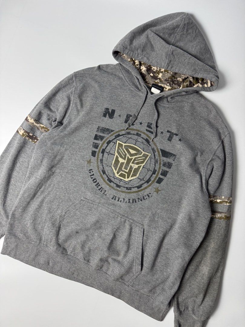 Universal Studios Transformers Global Alliance Grey Hoodie (Category: Hoodies) located in Cavite. Submitted by dracokidstuff (Listing ID 1456422337, Image 3). Description: - Grey hoodie with Transformers Global Alliance graphic - Features N.E.S.T. logo - Camouflage print lining inside the hood - Stripes and camo detail on the sleeves - Distressed 'T' design on the back graphic - Universal Studios branding on the tag - Ideal for any Transformers f