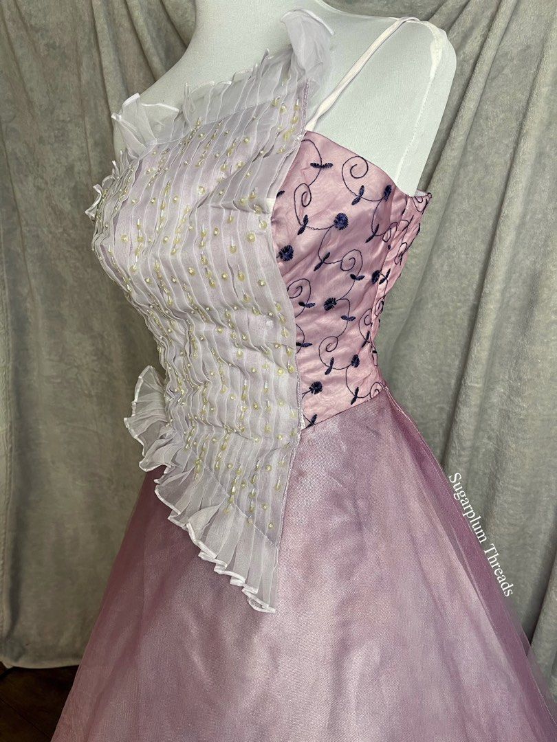 Purple Gown (Category: Evening dresses & gowns) located in Manila. Submitted by sugarplumthreadsph (Listing ID 1453369097, Image 2). Description: -Color & Palette: Features soft lavender and dusty pink undertones with contrasting dark navy blue embroidery and pearlescent embellishments. -Bodice Design: A two-part asymmetrical design: *The left side consists of a white/off-white semi-sheer pleated panel adorned with rows of faux pearl beads and fi