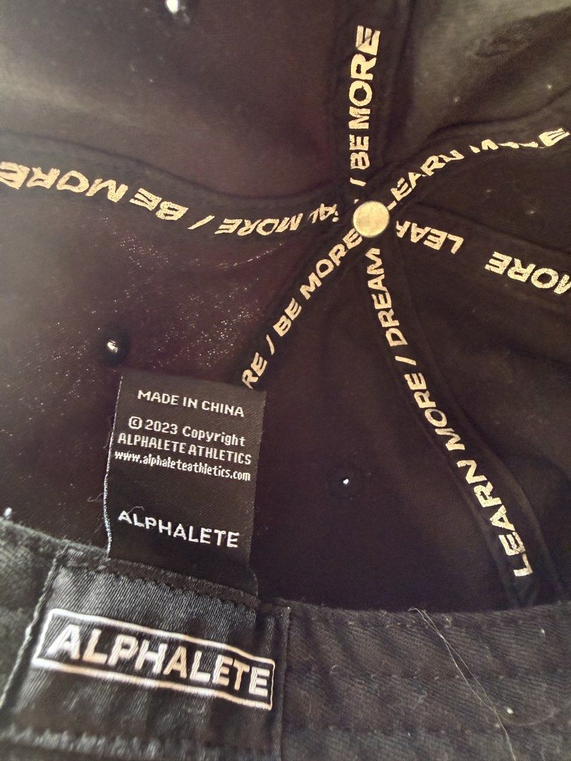 Alphalete Adjustable Cap / Hat Black (Category: Caps & Hats) located in Pasig City. Submitted by kfreed (Listing ID 1456681787, Image 2). Description: - Black ALPHALETE cap - Embroidered ALPHALETE logo on front - Inner lining with motivational phrases ('LEARN MORE / DREAM MORE / BE MORE') - Adjustable metal buckle for a custom fit - Made in China.