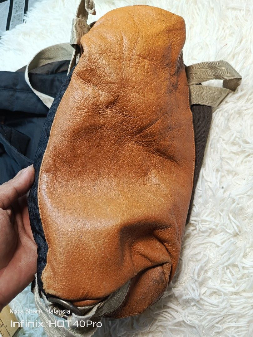 Backpack (Category: Backpacks) located in Kuala Lumpur. Submitted by grandturtle_dd5ca3 (Listing ID 1456687399, Image 3). Description: Material Composition: Heavyweight, durable brown canvas or cordura upper paired with a tan/brown suede leather bottom layer for extra structural protection. Lash Tabs / Pig Snouts: Two classic diamond-shaped leather accents sewn onto the upper front panel, historically used to tie down gear or cords. Branding: Fea