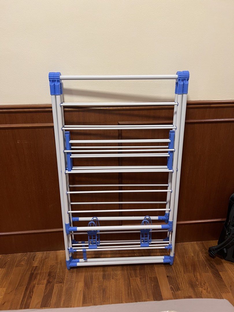 Foldable Drying Rack (Category: Clothes Drying Rack) located in Singapore. Submitted by hecarimshadowislessg (Listing ID 1456732308, Image 1). Description: ✅Price Negotiable ✅Pick up at Tiong Bahru - Foldable drying rack - Multiple hanging bars - White frame with blue plastic accents - Folds flat for easy storage - Sturdy construction - Ideal for laundry or airing items.
