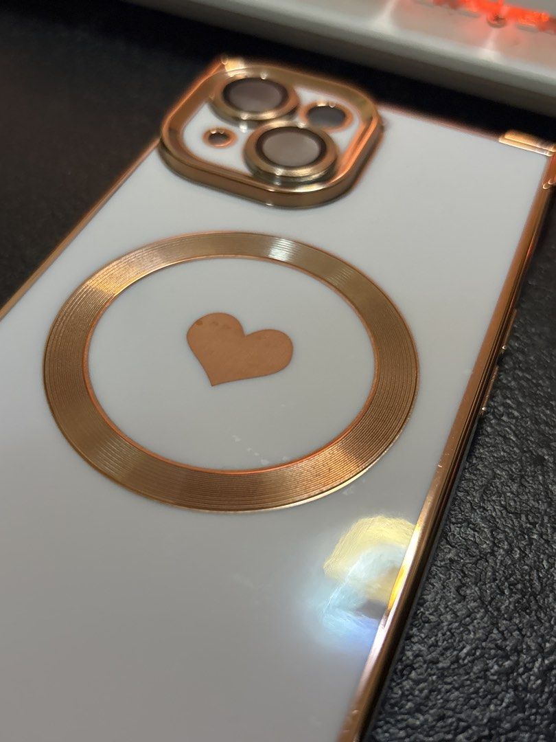 iPhone 15 case (Category: Cases & Sleeves) located in Malabon City. Submitted by luxgoals (Listing ID 1456785657, Image 2). Description: - Designed for iPhone 15 - Stylish white finish with rose gold accents - Features a cute heart design on the back - MagSafe compatible for easy charging and accessory attachment - Sleek and protective - Condition: 4/5 stars.