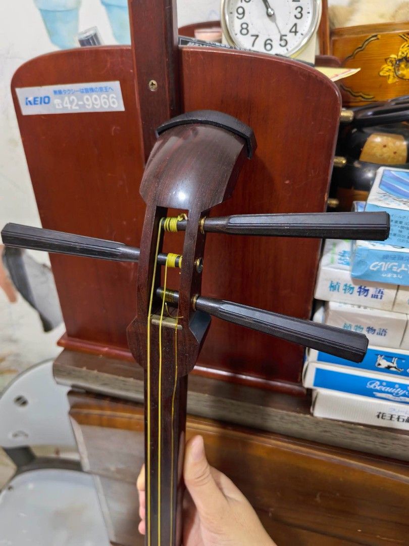 Japanese Shamisen (Category: Musical Instruments) located in Cebu City. Submitted by dudes_villanueva (Listing ID 1456910905, Image 3). Description: Japanese Shamisen 📌 Features a long, fretless wooden neck, three strings, and a square body with a torn skin membrane showing visible damage on the front face. (Back side skin damage also) 📌 The instrument includes tuning pegs at the head, a decorative body cover (do-kake) on the edge, and a promin