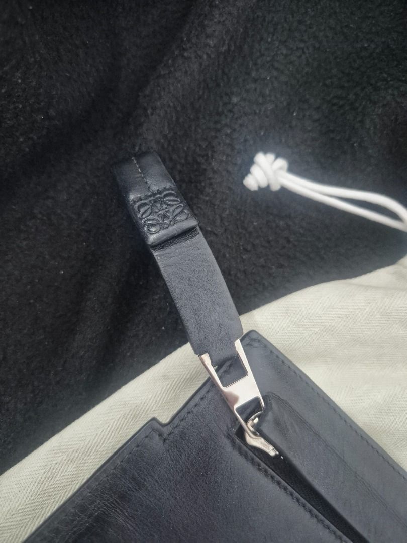 Prelove LOEWE Clutch (Category: Luxury Bags & Wallets) located in Caloocan City. Submitted by victorfrancis (Listing ID 1456950733, Image 2). Description: This image features a luxury leather pouch/clutch resting on its branded dust bag: ​Item: A black leather zip-top clutch or pouch by luxury fashion house Loewe. ​Details: ​Brand Markings: The iconic Loewe anagram logo is debossed in the bottom right corner of the black leather pouch, as well as