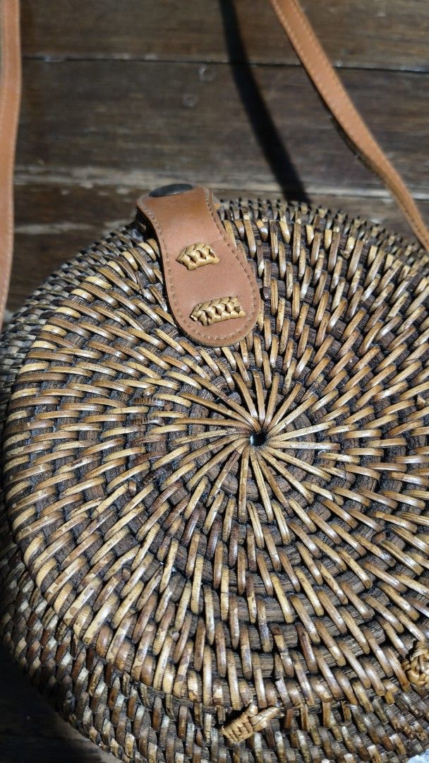 Rattan sling bag (Category: Cross-body Bags) located in Quezon City. Submitted by morningstar_52 (Listing ID 1456924975, Image 2). Description: - round rattan bag with minimal flaw - Features a brown leather strap and closure - Interior lined with vibrant, colorful batik fabric - Ideal for beach trips or casual outings - Unique woven design.