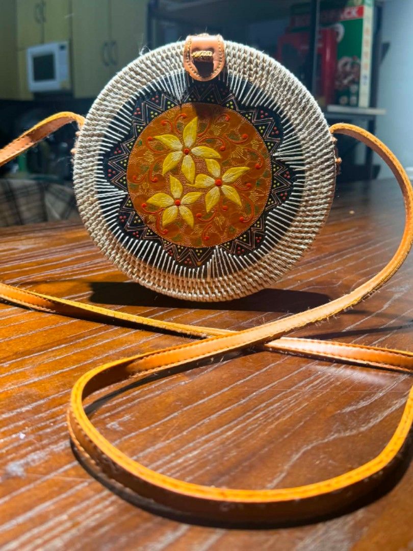 Round Rattan Bag with Batik Design (Category: Cross-body Bags) located in Manila. Submitted by thea_gabrielle (Listing ID 1456792823, Image 2). Description: Cute round rattan bag. Features a colorful batik-inspired floral design in the center. Tan leather strap and closure. Great for beach trips or casual outings. Unique woven texture..