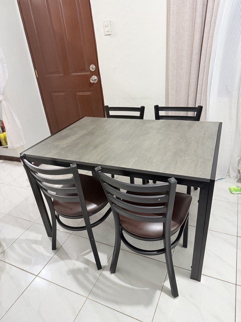 4-Seater Dining Table and Chairs Set (Category: Tables & Sets) located in Manila. Submitted by ellebarbacion (Listing ID 1457130200, Image 1). Description: - Compact dining set designed for small spaces - Table features a grey textured top and black metal frame - Includes four chairs with black metal frames - Chairs have comfortable brown faux leather seats - Perfect for kitchens or dining nooks - Easy to clean and maintain.