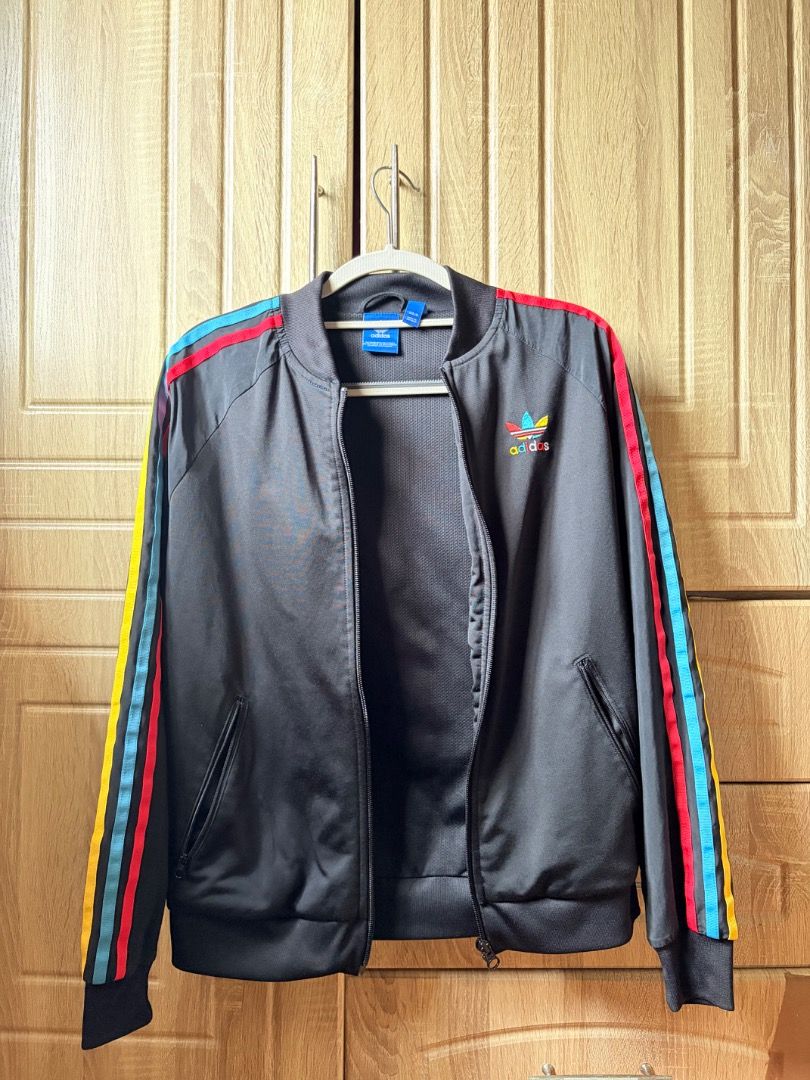 Adidas Track Jacket Rainbow Stripes (Category: Coats, Jackets and Outerwear) located in Tanza. Submitted by kmoarse (Listing ID 1457081947, Image 1). Description: - Classic Adidas track jacket - Color: Black - Iconic three stripes on sleeves (red, blue, yellow) - Rainbow Adidas logo on chest and back - Zip-up front - Features pockets - Ideal for casual wear or sports.