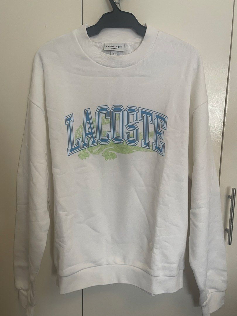Lacoste pullover/ sweatshirt (Category: Coats, Jackets and Outerwear) located in Manila. Submitted by alldayshoppinggirl (Listing ID 1457012802, Image 1). Description: 💯 ORIGINAL BRANDNEW WITH TAG STORE BOUGHT NEGOTIABLE White Lacoste loose-fit fleece crewneck sweatshirt featuring a large collegiate-style blue block logo layered over a green crocodile graphic on the chest. Neckline is Classic ribbed crewneck collar with a visible brand tag while