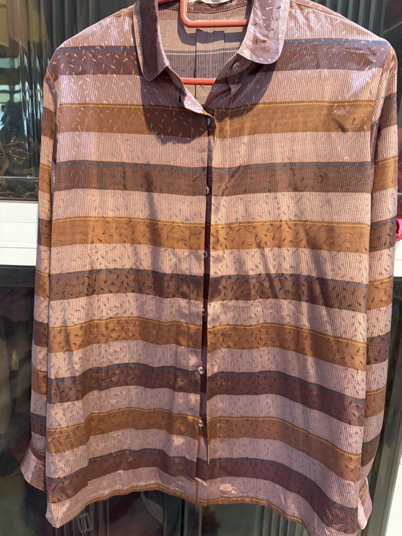 Striped Button-Up Blouse (Category: Blouses) located in Kuala Lumpur. Submitted by danishmyra (Listing ID 1457044708, Image 1). Description: - Long-sleeved button-up blouse - Horizontal stripes in brown, pink, and blue - Fabric with subtle sheen and textured pattern - Classic collar and button front - Versatile for layering or wearing solo.