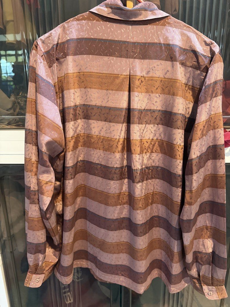 Striped Button-Up Blouse (Category: Blouses) located in Kuala Lumpur. Submitted by danishmyra (Listing ID 1457044708, Image 2). Description: - Long-sleeved button-up blouse - Horizontal stripes in brown, pink, and blue - Fabric with subtle sheen and textured pattern - Classic collar and button front - Versatile for layering or wearing solo.