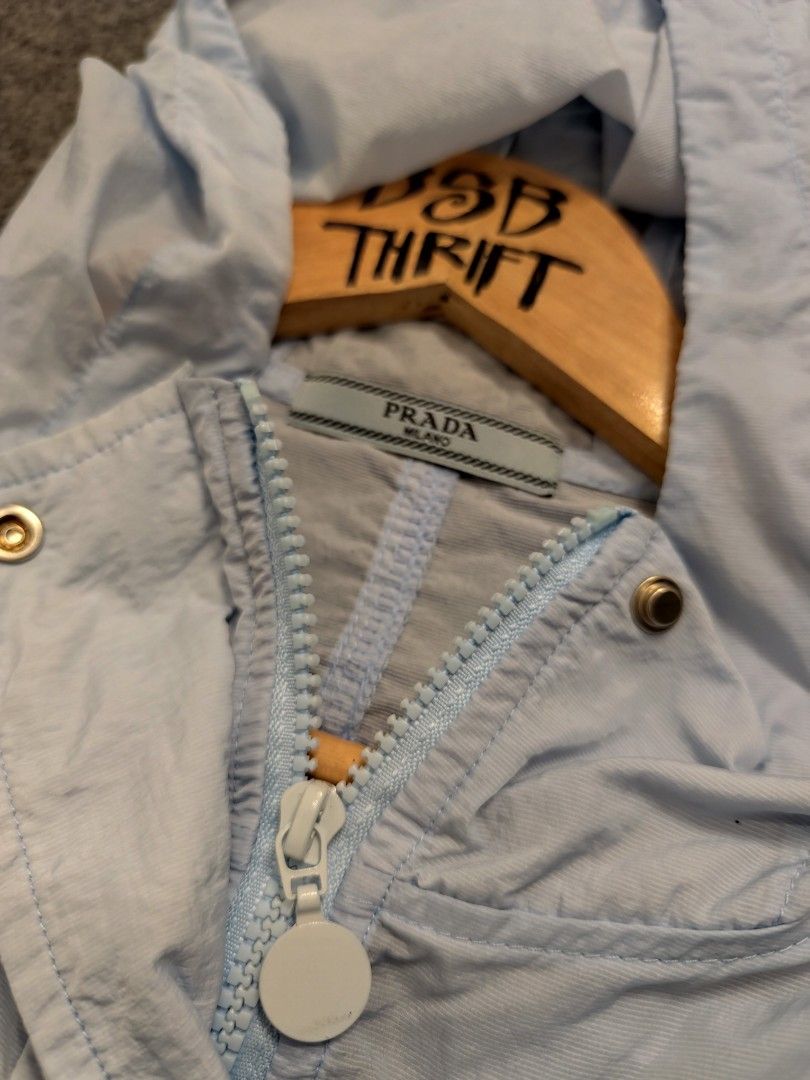 Prada Light Blue Hooded Windbreaker Jacket (Category: Luxury Apparel) located in Cordova. Submitted by bsb.streetluxvintage.clothing (Listing ID 1457259530, Image 3). Description: - Light blue Prada windbreaker jacket - Hooded design with drawstring hem - Two front pockets - Zip-up closure - Iconic Prada triangle logo on chest - Ideal for casual wear or light outdoor activities.