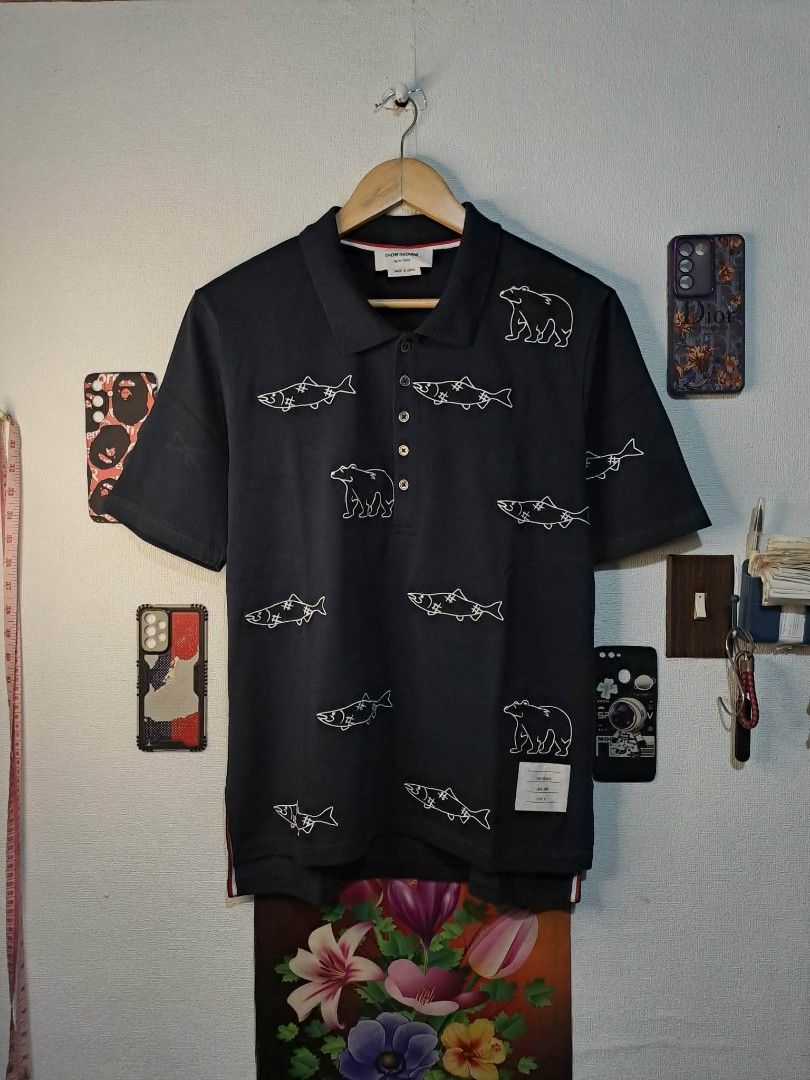 Thom Browne Bear and Salmon (Category: Luxury Apparel) located in Manila. Submitted by yaseen_73 (Listing ID 1457143117, Image 1). Description: Authentic Thom Browne Bear and Salmon Embroidered Polo Shirt, specifically featuring an all-over cartoon-style line embroidery of grizzly bears and stitched salmon Made in Japan Wearing Size : No. 2 Dimensions : W20 L26'27 Color Rate : 9.9/10 With Stain Issue Needs Proper Hand Wash (See Last Photo) No Lin