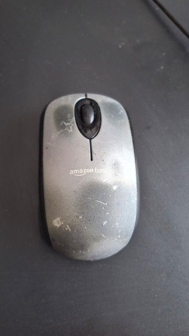 Amazon Basics Wireless Computer Mouse (Category: Mouse & Mousepads) located in Singapore. Submitted by mfibp (Listing ID 1457370230, Image 1). Description: - Amazon Basics wireless computer mouse - Color: Silver with black scroll wheel - Condition: Shows signs of wear and tear from regular use - Functionality: Still works great - Ideal for: Everyday computer tasks.