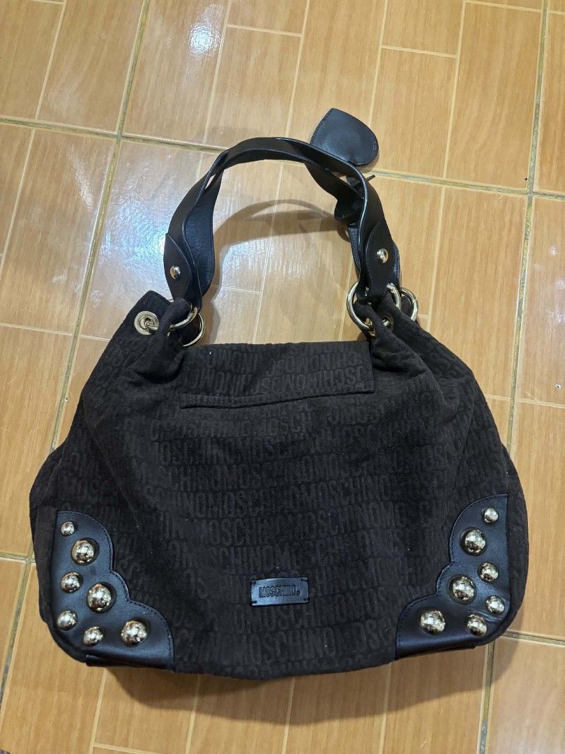 Brown Moschino Monogram Shoulder Bag with Studs (Category: Luxury Bags & Wallets) located in Paranaque City. Submitted by poego (Listing ID 1457449026, Image 2). Description: - Authentic Moschino shoulder bag in classic brown. - Features the signature all-over monogram pattern. - Accented with stylish black leather trim and elegant gold-tone studs. - Offers a spacious interior with a convenient zippered pocket for essentials. - Equipped with doub