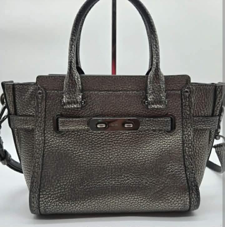 Coach Metallic Pebble Leather Satchel Handbag (Category: Luxury Bags & Wallets) located in Cabanatuan. Submitted by almaespino24263 (Listing ID 1457412985, Image 1). Description: - Metallic pewter-colored Coach satchel - Pebbled leather exterior - Secure turn-lock closure on the front - Interior zip pocket and additional compartments - Comfortable top handles - Includes a detachable shoulder strap for versatile carrying - Ideal size for everyday 