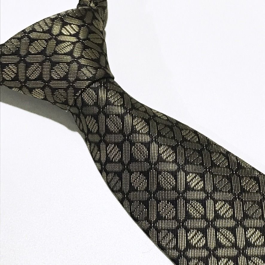 D'URBAN Black Repeating Geometric Textured Neck Tie (Category: Ties) located in Taguig. Submitted by retrogaze (Listing ID 1457368695, Image 1). Description: This 100% polyester necktie by D'URBAN features a deep black base woven with a crisp, structured stiffness. The body displays a dense, repeating geometric lattice pattern of interlocking circular and oval links highlighted in metallic champagne-gold thread against the dark ground. Recommende