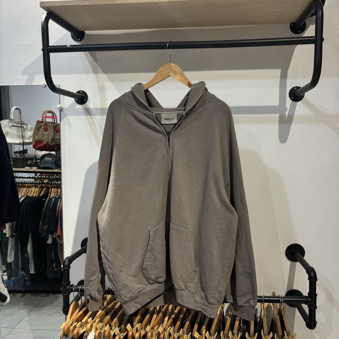Essentials Zip up Jacket (Category: Coats, Jackets and Outerwear) located in Bambang. Submitted by heats777 (Listing ID 1457442089, Image 2). Description: - Brand: Essentials - Type: Zip-up Jacket - Size: XL (US 44 / UK 44 / EU 54) - Color: Taupe - Features: Soft material, full zip closure, hood, front pockets, 'Essentials' logo on back and sleeve. - Condition: Great.