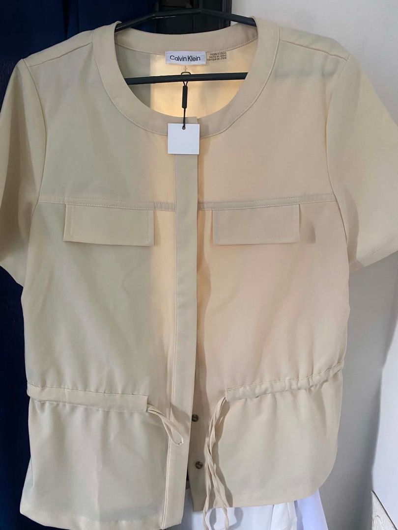 Calvin Klein Cream Short Sleeve Top Size S (Category: Blouses) located in Arayat. Submitted by ipogladys (Listing ID 1457640413, Image 2). Description: - Brand: Calvin Klein (authentic) - Size: S (fits large body frame) - Neckline: Round - Closure: Button-up front - Pockets: Two chest pockets - Feature: Drawstring waist RFS: wrong size .