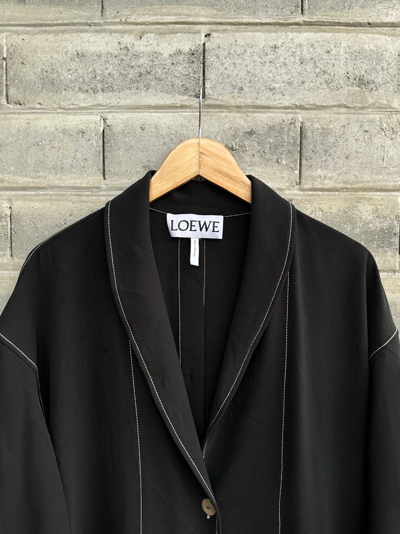 LOEWE Contrast White Stitching Black Long Duster Coat (Category: Luxury Apparel) located in Urdaneta. Submitted by redeemedcollective (Listing ID 1457831603, Image 3). Description: An avant-garde, structural statement piece from LOEWE. This black long coat/cardigan dress features distinct white contrast topstitching, elegant shawl lapels, engraved horn buttons, large utility patch pockets, and unique tie-knot details at the cuffs. A versatile gar