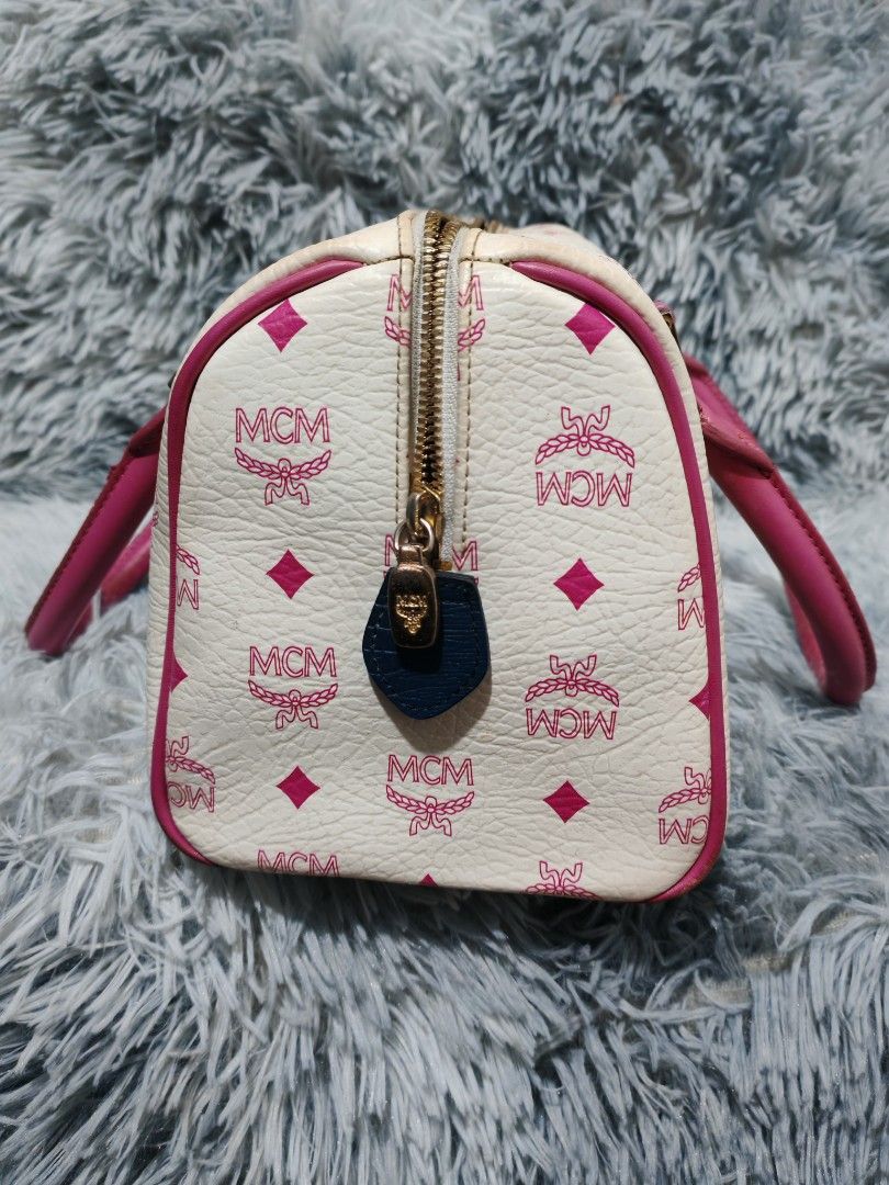 MCM White Monogrammed Boston Bag with Pink Trim (Category: Luxury Bags & Wallets) located in Manila. Submitted by camellesal67218 (Listing ID 1457769812, Image 3). Description: - White MCM Boston bag with signature monogram print. - Pink leather trim and handles. - Central lion emblem with colorful patches. - Zipper closure. - Interior: 1 zippered pocket, 1 slip pocket. - Exterior shows some signs of wear. - Interior is clean..