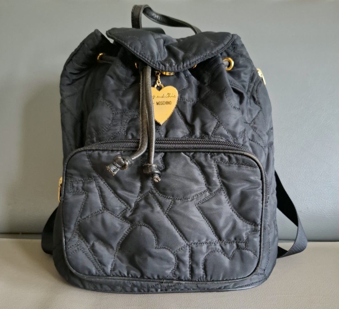 Moschino Cheap and Chic Quilted Heart Black Backpack (Category: Backpacks) located in Don Carlos. Submitted by PphiXi_Finds (Listing ID 1457805638, Image 1). Description: Black quilted backpack with heart pattern. Gold hardware details. Front zip pocket and main drawstring closure. Adjustable shoulder straps. Includes a cute heart charm with 'Cheap and Chic by Moschino' engraving. Great for everyday use..
