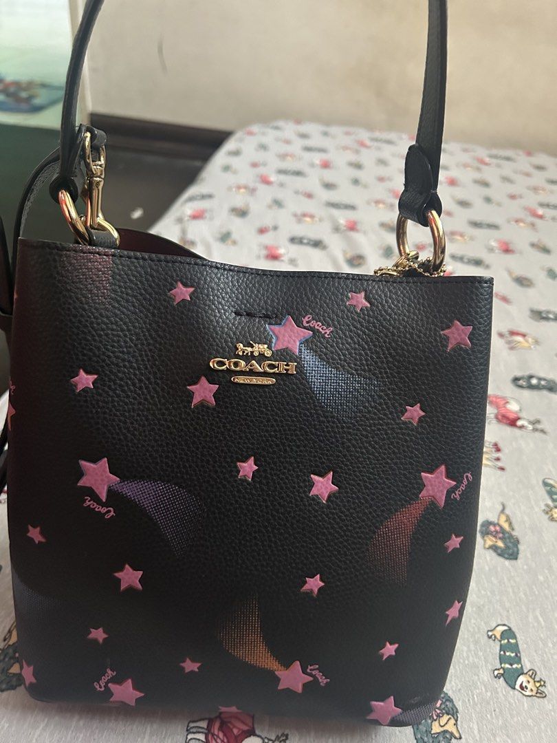 Coach Black Star Print Bucket Bag (Category: Luxury Bags & Wallets) located in Manila. Submitted by lottiepot (Listing ID 1457909001, Image 1). Description: - Adorable black Coach bucket bag - Features a fun pink star print - Includes both a top handle and a crossbody strap for versatile carrying - Elegant gold hardware details - Secure zipper closure - Ideal for your everyday essentials and style.