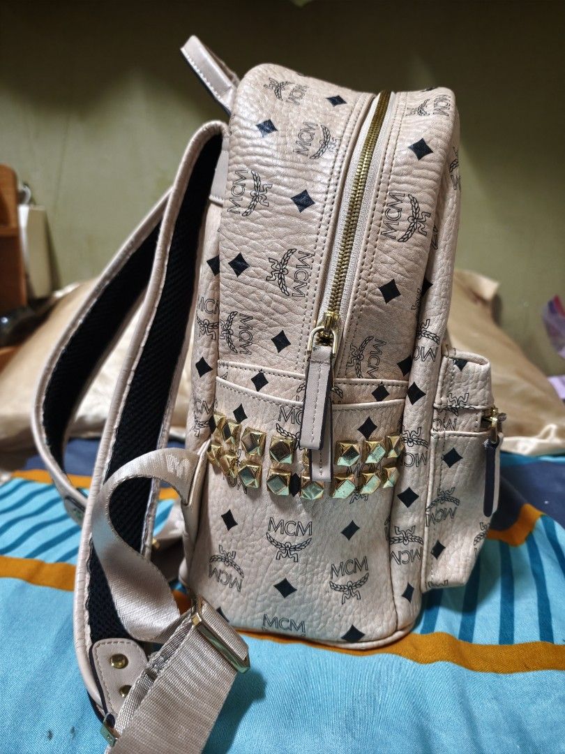 MCM Stark Backpack MM Beige Visetos Studded (Category: Luxury Bags & Wallets) located in Makati City. Submitted by manririn (Listing ID 1458049217, Image 3). Description: - MCM Stark Backpack - Classic Beige Visetos Print - 16k Gold Studs on side Pocket - Adjustable Straps - Main Compartment + Inner Pocket - Ideal for Everyday Use ISSUE: The clothing is damaged around the small front zipper, with visible tearing and fraying of the fabric along th