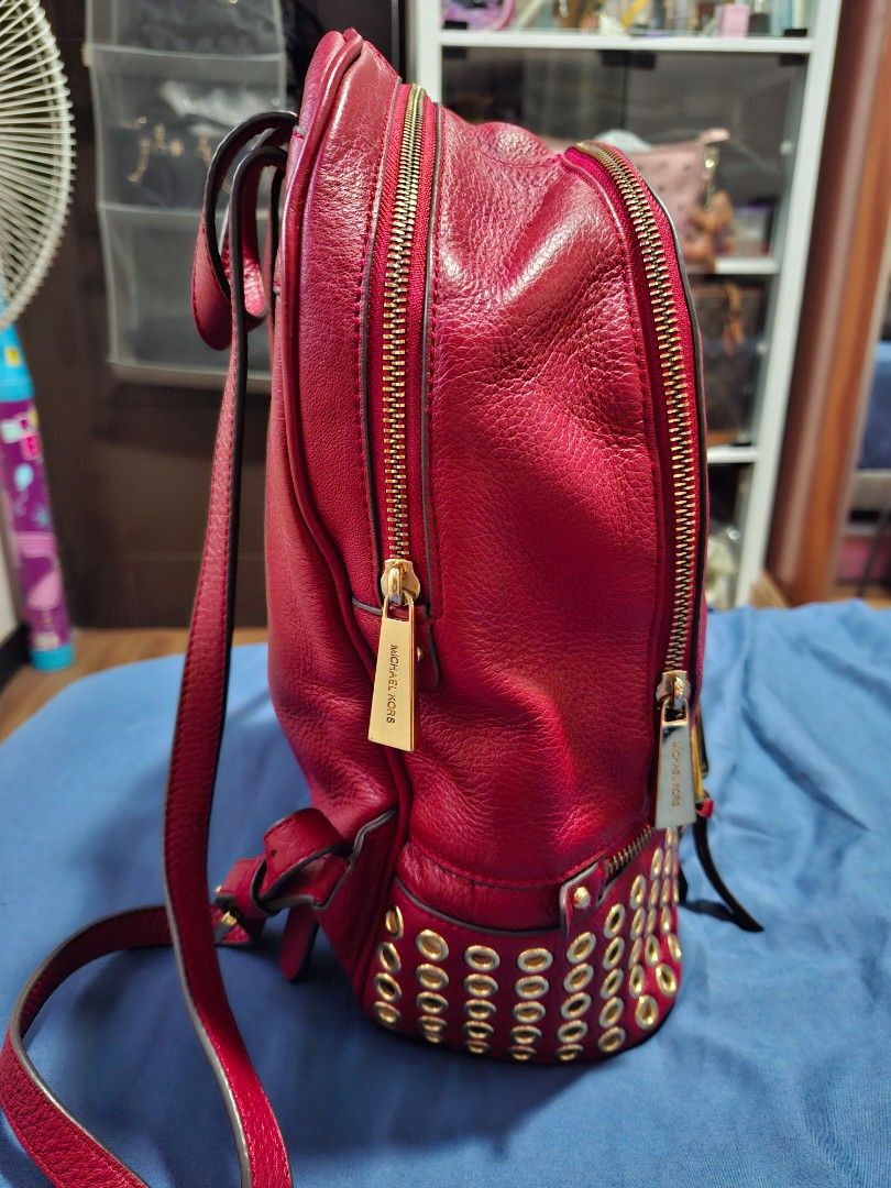 Michael Kors Red Leather Studded Backpack (Category: Backpacks) located in Manila. Submitted by yanakolekzione (Listing ID 1458063864, Image 2). Description: - Authentic Michael Kors backpack in a striking red color. - Crafted from genuine leather with elegant gold stud accents on zippers. - Interior boasts multiple compartments, including a secure zippered pocket. - Adjustable straps for a comfortable, customized fit. - Please note: Minor signs 