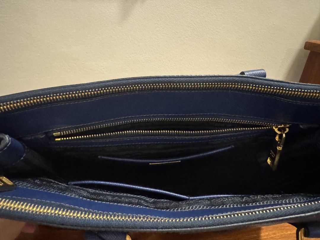 Prada Saffiano Tote Bag Navy Blue (Category: Luxury Bags & Wallets) located in Quezon City. Submitted by newbieandoldie (Listing ID 1457998669, Image 2). Description: - Classic Prada tote in navy blue Saffiano leather. - Elegant gold hardware details. - Interior includes a zip pocket and slip pockets for organization. - Note: Handles show some wear and tear. - Corners have minor scuff marks. - Still a fantastic and durable bag for daily use..