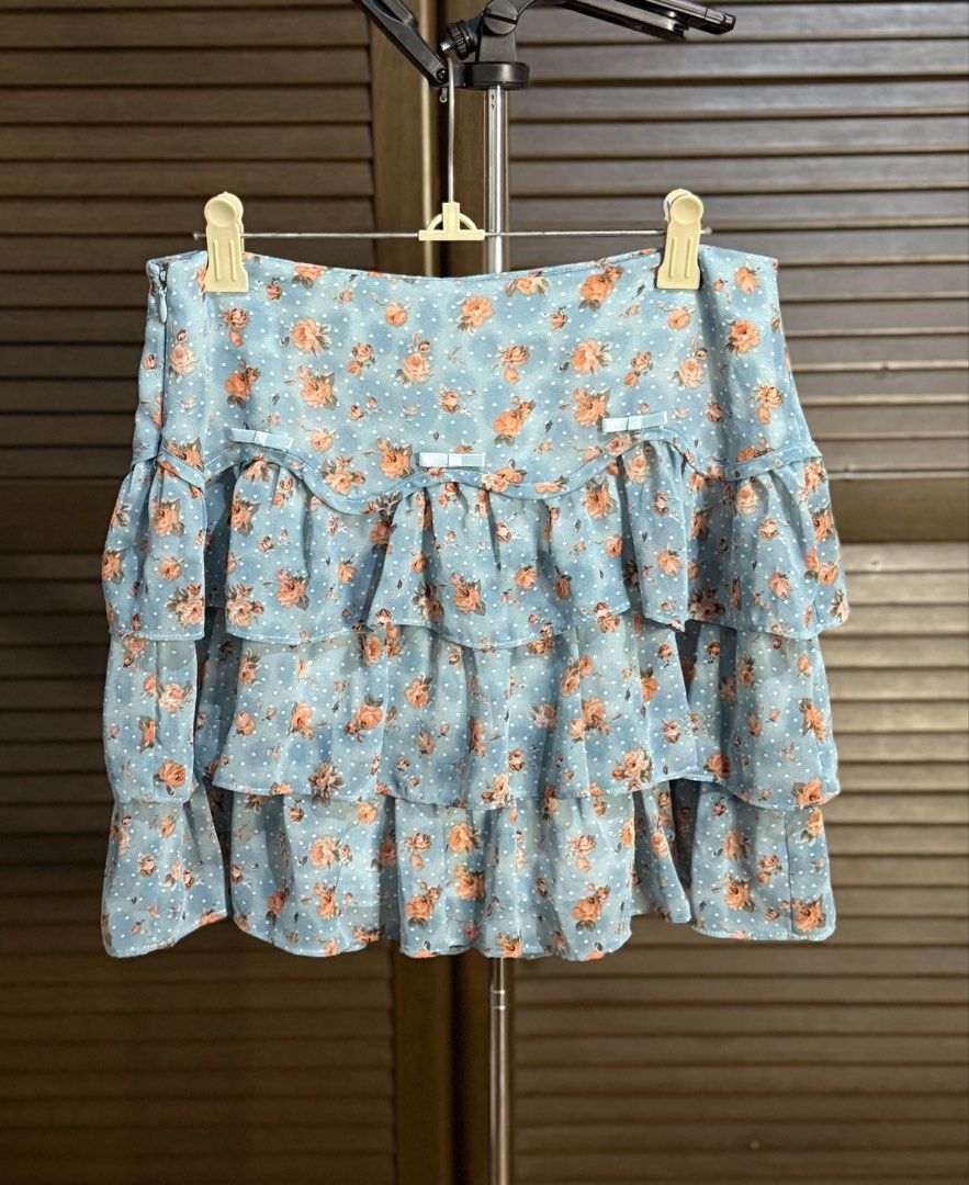 Blue Floral Ruffle Tiered Mini Skirt (Category: Skirts) located in Santiago. Submitted by ashley.collection (Listing ID 1458108713, Image 1). Description: - Adorable blue mini skirt with a charming floral print. - Features multiple tiers of ruffles for a playful look. - Accented with small white polka dots and cute white bows on the waistband. - Made from lightweight fabric, perfect for comfortable wear. - Ideal for creating a sweet and feminine 