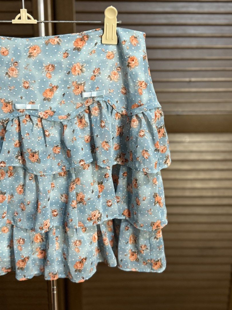 Blue Floral Ruffle Tiered Mini Skirt (Category: Skirts) located in Santiago. Submitted by ashley.collection (Listing ID 1458108713, Image 2). Description: - Adorable blue mini skirt with a charming floral print. - Features multiple tiers of ruffles for a playful look. - Accented with small white polka dots and cute white bows on the waistband. - Made from lightweight fabric, perfect for comfortable wear. - Ideal for creating a sweet and feminine 