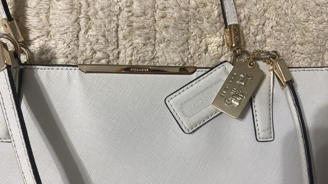Coach White Saffiano Leather Tote Bag (Category: Luxury Bags & Wallets) located in Angono. Submitted by denflrntz (Listing ID 1458237731, Image 2). Description: - White Coach tote bag bought for Php 15k (Duty Free - Korea) - Saffiano leather exterior - Gold hardware details - Interior zip pocket - Small black stain in the back (visible in last photo) - Clean interior - Spacious design - Slightly negotiable.