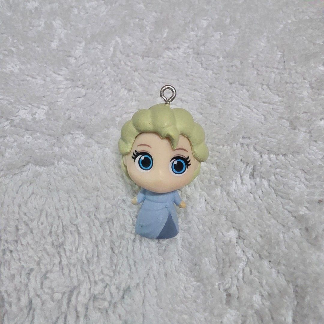 Elsa Disney Frozen Phone Charm (Category: Character Goods) located in Pasig City. Submitted by aerasdrafts (Listing ID 1458267152, Image 1). Description: Character: Elsa, the Snow Queen, recognizable by her pale blonde hair swept back into her iconic braid and her light blue dress. Format: A small vinyl or rubber mini-figure designed as a deformed/chibi (deforme) charm, featuring an eyelet screw at the top meant for attaching a keychain loop or a