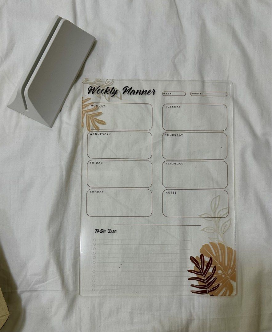 Acrylic Weekly Planner with Stand (Category: Stationery & School Supplies) located in Bulacan. Submitted by enha4lyf (Listing ID 1458414632, Image 2). Description: - Clear acrylic weekly planner - Includes a stand for easy display - Sections for each day of the week - Dedicated space for notes and a to-do list - Helps you organize your schedule effectively - Comes with a marker/eraser holder - Features a beautiful tropical leaf design.