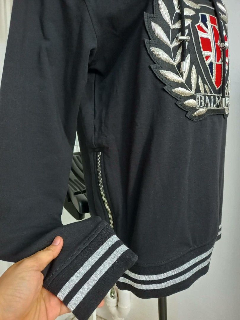 Balmain Black Hoodie with Crest Logo (Category: Hoodies) located in General Mariano Alvarez. Submitted by deslacbayan (Listing ID 1458324810, Image 2). Description: - Authentic Balmain black hoodie - Features a cool embroidered crest logo with the Balmain name - Stylish side zippers for added detail and functionality - Striped details on cuffs and hem for a sporty look - Brand new with tags still attached Large on tag (21.5x27.