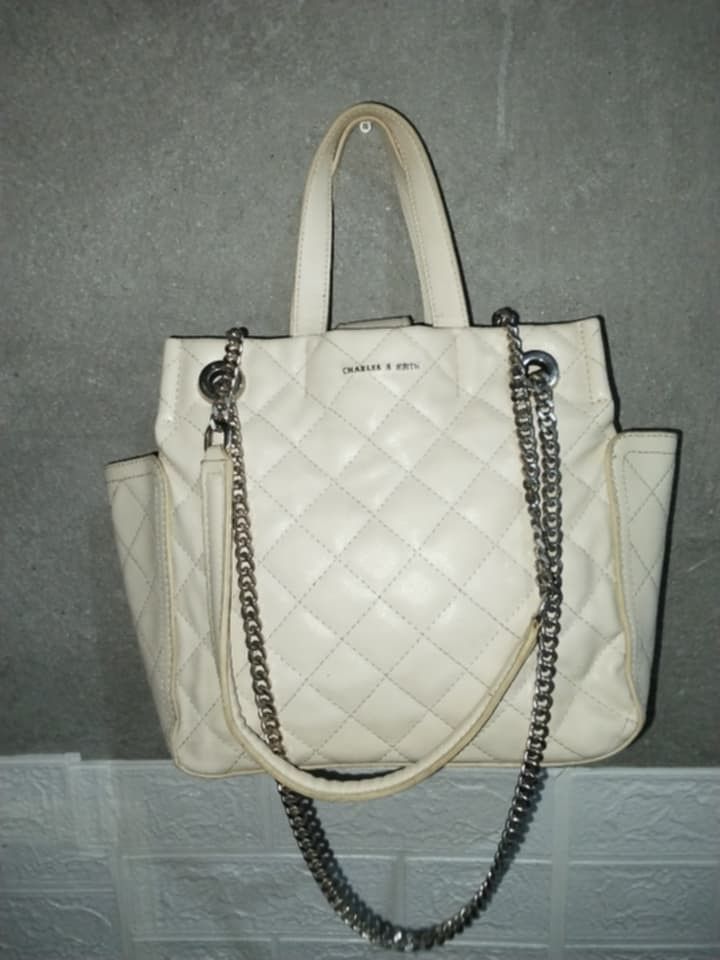 Charles & Keith Quilted Chain Handbag (Category: Luxury Bags & Wallets) located in Manila. Submitted by bagelyascollection (Listing ID 1458462314, Image 1). Description: - Cream colored quilted handbag by Charles & Keith - Elegant silver chain straps and handles - Convenient side pockets for quick access - Secure zippered interior compartment - Protective metal studs on the bottom - Note: Minor marks present inside the bag.