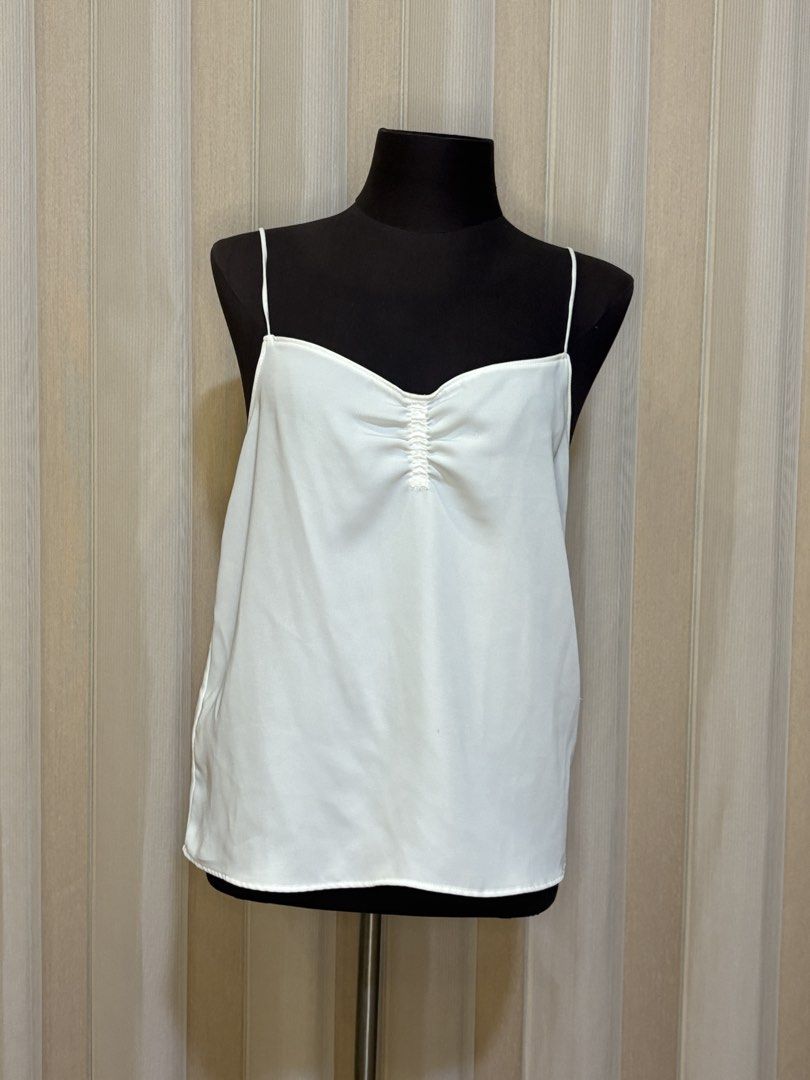 Mango White Camisole Top (Category: Sleeveless) located in Angeles City. Submitted by shopbettina (Listing ID 1458408992, Image 1). Description: - White camisole top from Mango Suit - Features thin spaghetti straps - Ruched detail at the bust - Small mark on fabric (shown in last photo) - Versatile for layering or wearing alone.