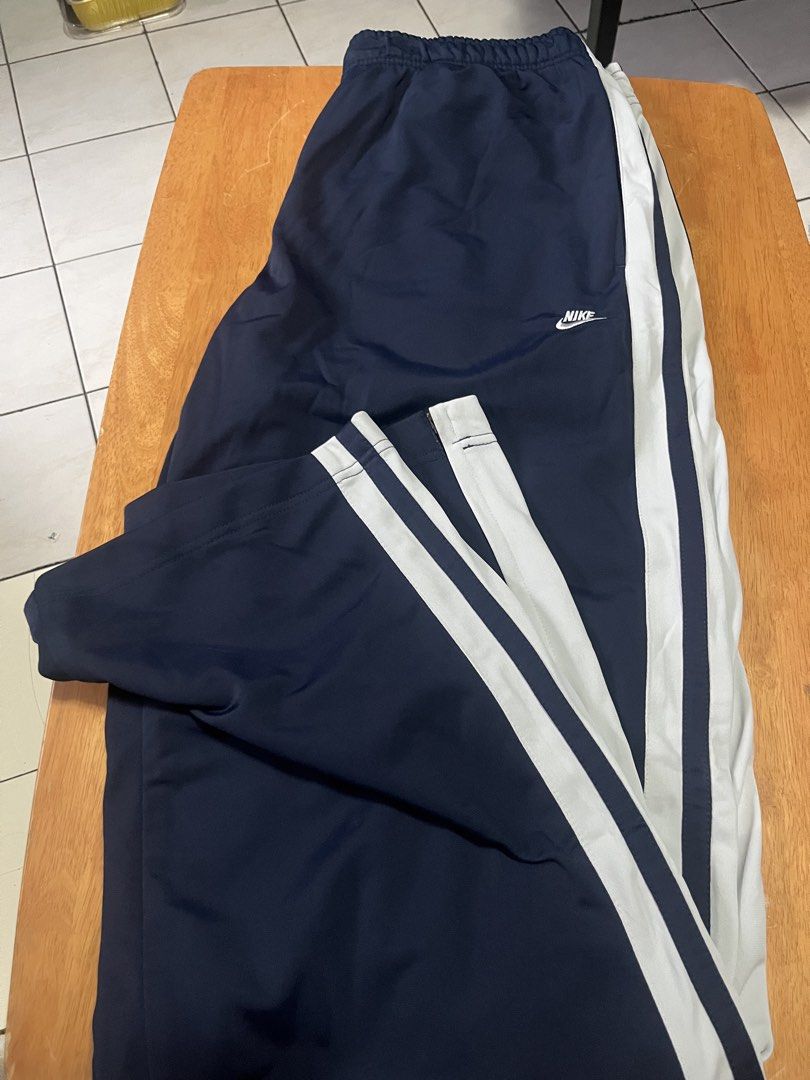 Nike track pants (Category: Joggers) located in Quezon City. Submitted by shopaholics.31 (Listing ID 1458310281, Image 2). Description: The highlighted item is a pair of vintage Nike side-stripe track pants in navy blue and white. Color Scheme: Deep midnight navy blue with stark contrast white side stripes.Branding: Classic mini Nike Swoosh text logo embroidered in white on the left thigh. Design Details: White dual-stripe panelling running down 