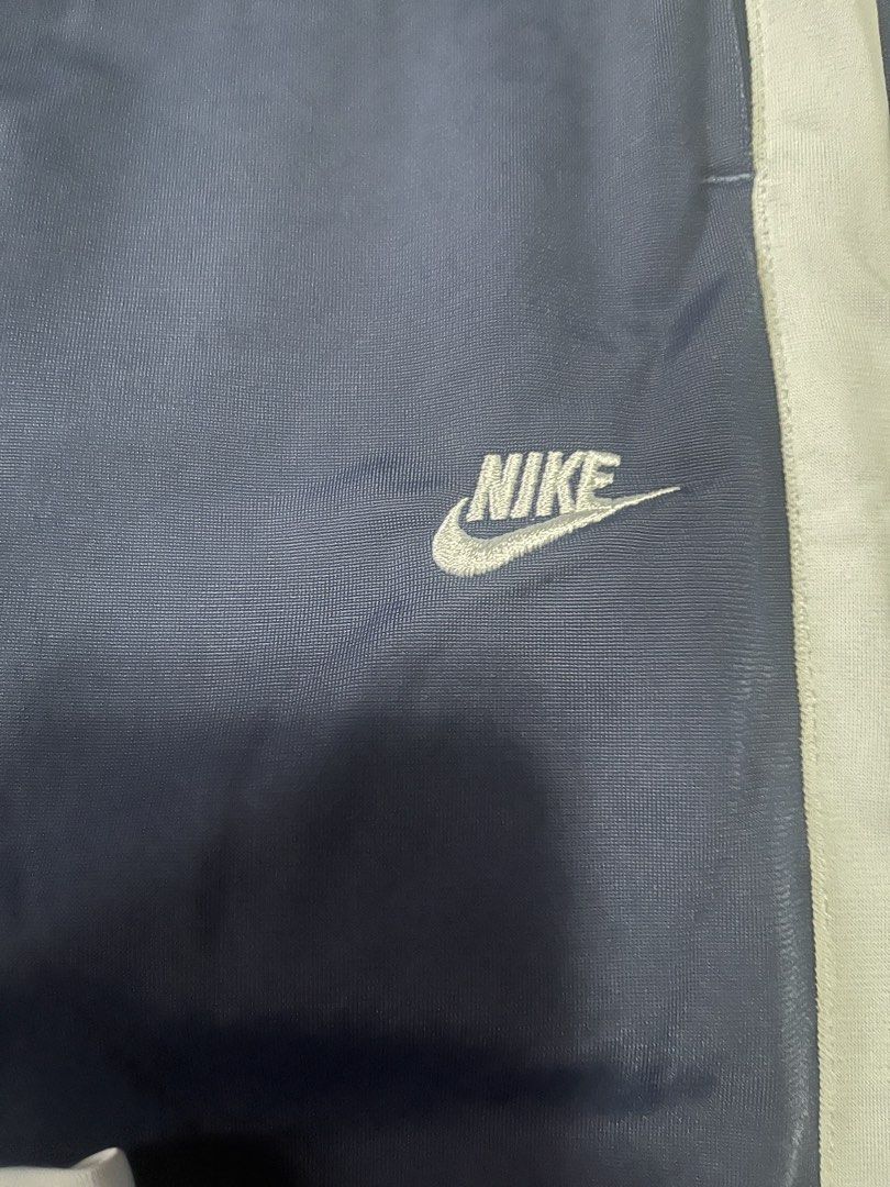 Nike track pants (Category: Joggers) located in Quezon City. Submitted by shopaholics.31 (Listing ID 1458310281, Image 3). Description: The highlighted item is a pair of vintage Nike side-stripe track pants in navy blue and white. Color Scheme: Deep midnight navy blue with stark contrast white side stripes.Branding: Classic mini Nike Swoosh text logo embroidered in white on the left thigh. Design Details: White dual-stripe panelling running down 