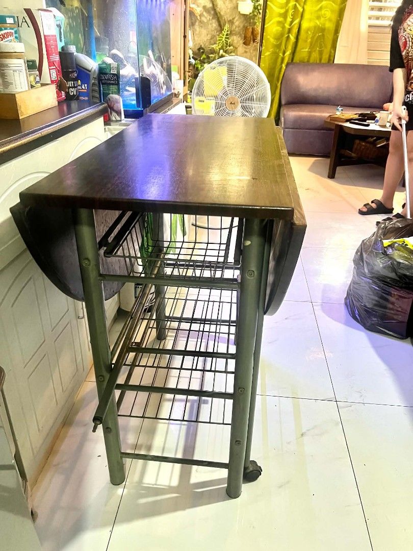 Extendable Dining Table w/ storage (Category: Tables & Sets) located in Pasig City. Submitted by tessdelrosario (Listing ID 1453456785, Image 3). Description: preloved Extendable dining table with s- *Top*: Dark wood, foldable sides so you can make it smaller or bigger - *Base*: Metal frame with wheels , plus shelves and a wine bottle rack underneath - *Vibe*: Super practical for small kitchens or condos Width 33inches Length when expanded 110inc