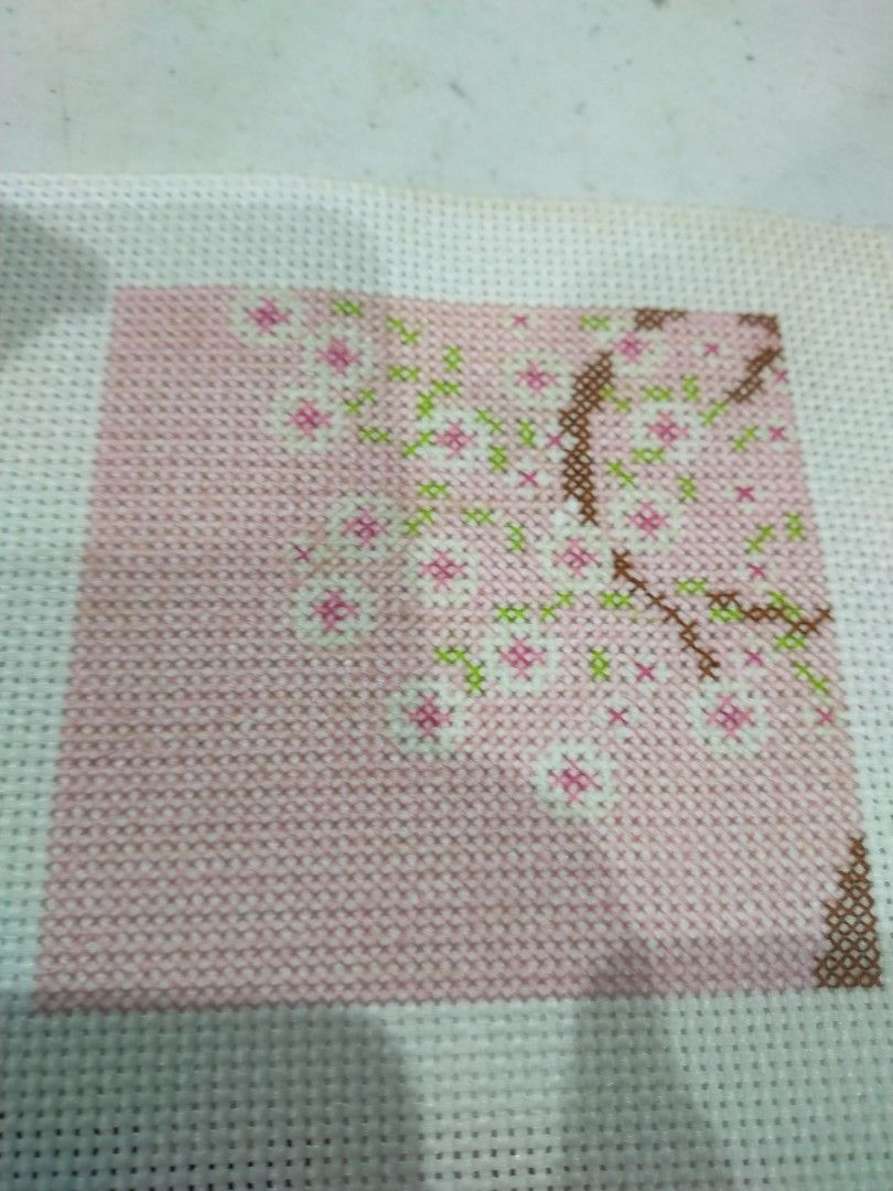 Unfinished Cross-stitch Cherry Blossom Design (Category: Handmade Craft) located in Pagadian. Submitted by kimygo (Listing ID 1453558846, Image 1). Description: - finished cross-stitch project - Features a pink background - Cherry blossom branch design - White canvas with grid pattern - Ideal for needlework enthusiasts.