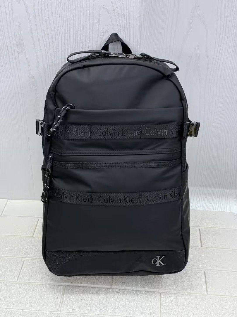 Calvin Klein Utility Backpack (Category: Backpacks) located in Mandaluyong City. Submitted by apparel_jenjo (Listing ID 1458798593, Image 1). Description: Color & Material: The backpack is built from a smooth, water-resistant matte black nylon fabric, giving it a premium and clean appearance. Branding: It features distinctive tonal Calvin Klein repeat-text branded ribbons across the front horizontal zipper areas, along with a metallic, silver-out