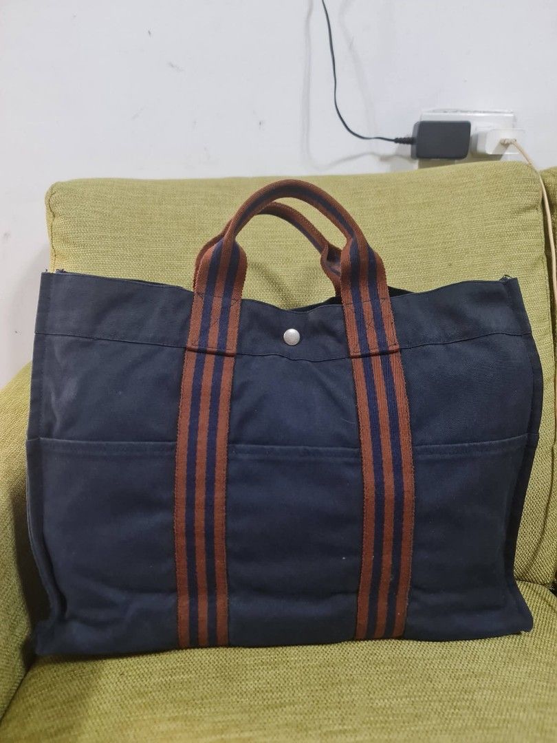 Hermes Paris Navy Canvas Tote Bag (Category: Luxury Bags & Wallets) located in Paombong. Submitted by dosbagshop (Listing ID 1458757870, Image 2). Description: - Authentic - Classic navy canvas tote from Hermes Paris - Features iconic striped handles - Ample interior space - Convenient exterior pockets - Ideal for everyday use or travel - A timeless and versatile accessory.