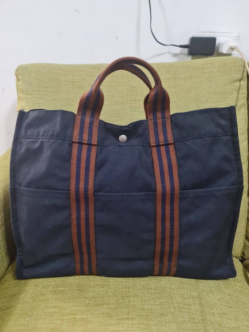 Hermes Paris Navy Canvas Tote Bag (Category: Luxury Bags & Wallets) located in Paombong. Submitted by dosbagshop (Listing ID 1458757870, Image 1). Description: - Authentic - Classic navy canvas tote from Hermes Paris - Features iconic striped handles - Ample interior space - Convenient exterior pockets - Ideal for everyday use or travel - A timeless and versatile accessory.