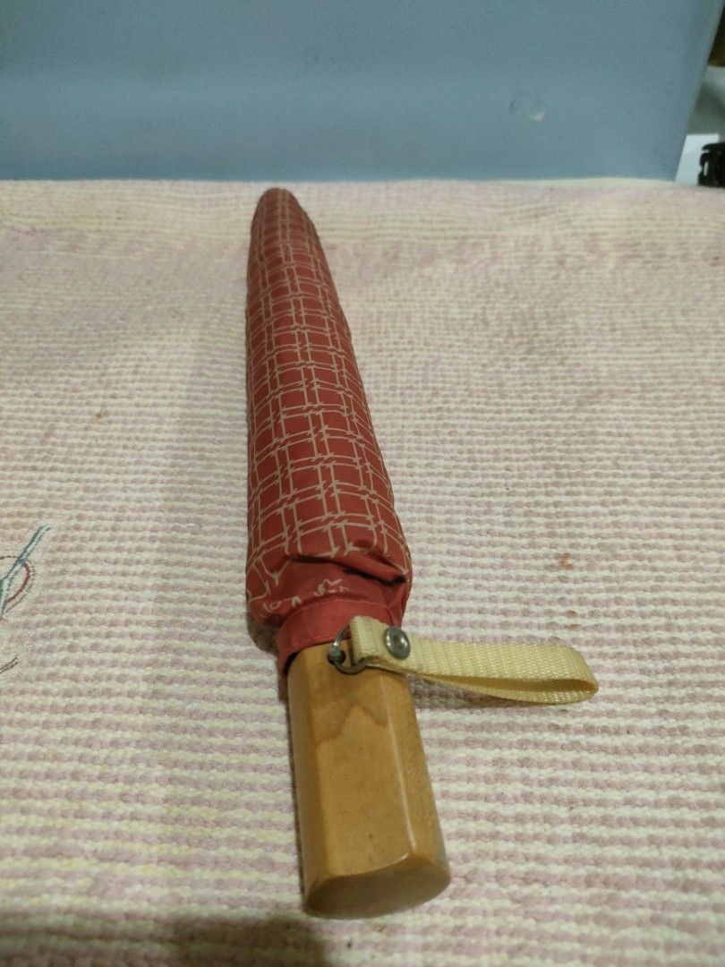 Hogan U.S.A. Red Patterned Folding Umbrella (Category: Umbrellas) located in Bulacan. Submitted by hunterherojapanjdm (Listing ID 1458834327, Image 2). Description: - Red folding umbrella with a stylish geometric pattern. - Features a classic wooden handle with the Hogan U.S.A. logo. - Compact and portable design, perfect for on-the-go. - Secure snap closure strap for easy fastening. - Effortlessly fits into your bag for convenient storage..