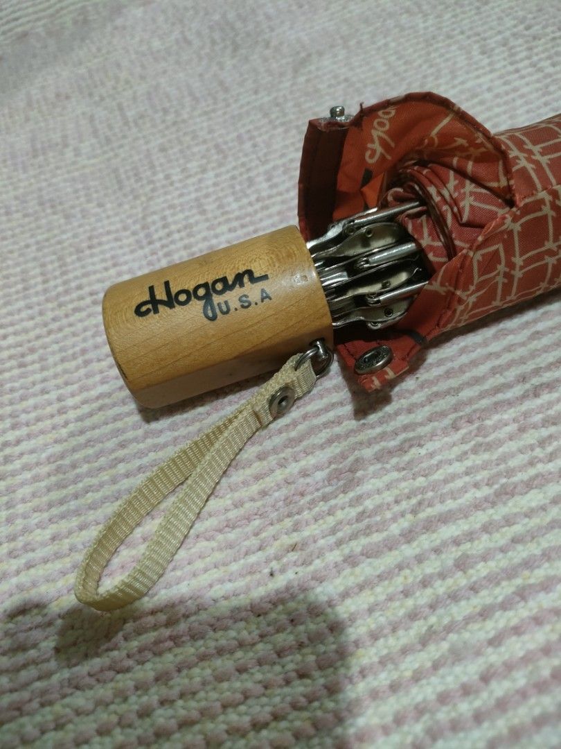 Hogan U.S.A. Red Patterned Folding Umbrella (Category: Umbrellas) located in Bulacan. Submitted by hunterherojapanjdm (Listing ID 1458834327, Image 3). Description: - Red folding umbrella with a stylish geometric pattern. - Features a classic wooden handle with the Hogan U.S.A. logo. - Compact and portable design, perfect for on-the-go. - Secure snap closure strap for easy fastening. - Effortlessly fits into your bag for convenient storage..