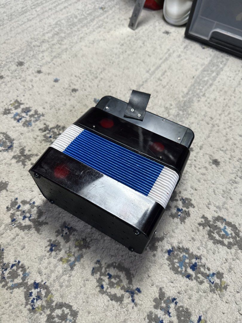 Mini Accordion Toy Musical Instrument (Category: Kids Toys) located in Daet. Submitted by thrifthings2018 (Listing ID 1458773365, Image 3). Description: - Black toy accordion, perfect for kids! - Vibrant red, white, and blue bellows for a fun look. - White buttons on top and bottom for easy play. - Includes a small strap on top. - Measures approximately 7 inches tall. - Great for sparking musical creativity!.