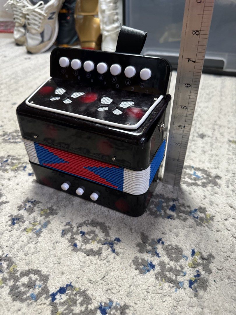 Mini Accordion Toy Musical Instrument (Category: Kids Toys) located in Daet. Submitted by thrifthings2018 (Listing ID 1458773365, Image 1). Description: - Black toy accordion, perfect for kids! - Vibrant red, white, and blue bellows for a fun look. - White buttons on top and bottom for easy play. - Includes a small strap on top. - Measures approximately 7 inches tall. - Great for sparking musical creativity!.