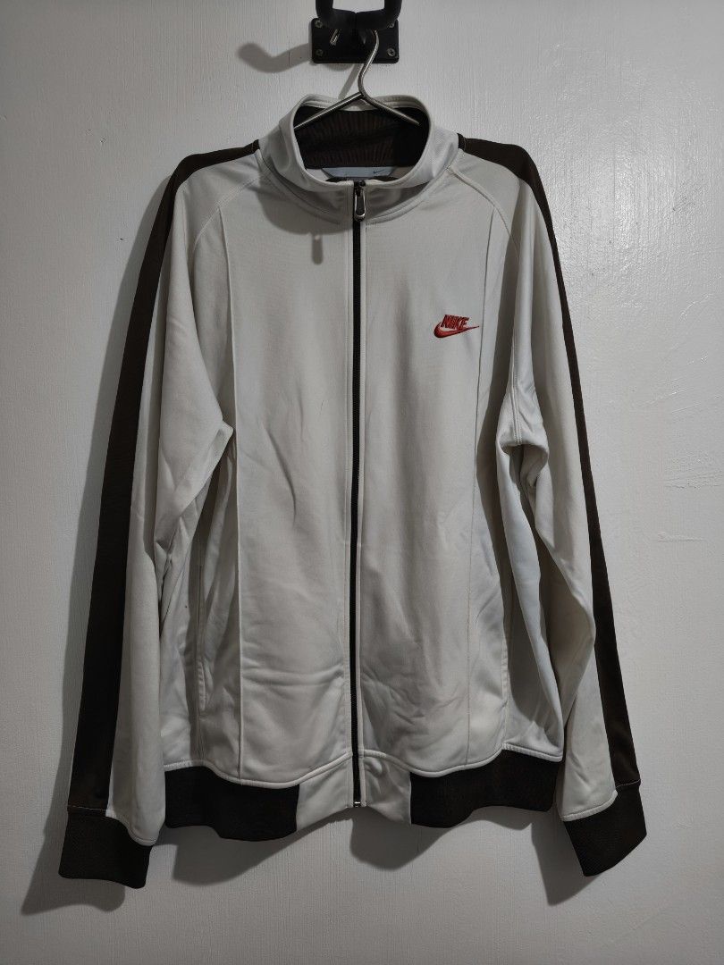 Nike Track Jacket White Brown Zip Up (Category: Coats, Jackets and Outerwear) located in Manila. Submitted by bmsthrift (Listing ID 1458762480, Image 1). Description: - White Nike track jacket - Brown accents on sleeves and hem - Full zip closure with YKK zipper - Small red Nike logo on chest - Minor marks on fabric (see close-up photos) - Perfect for casual wear or sports.